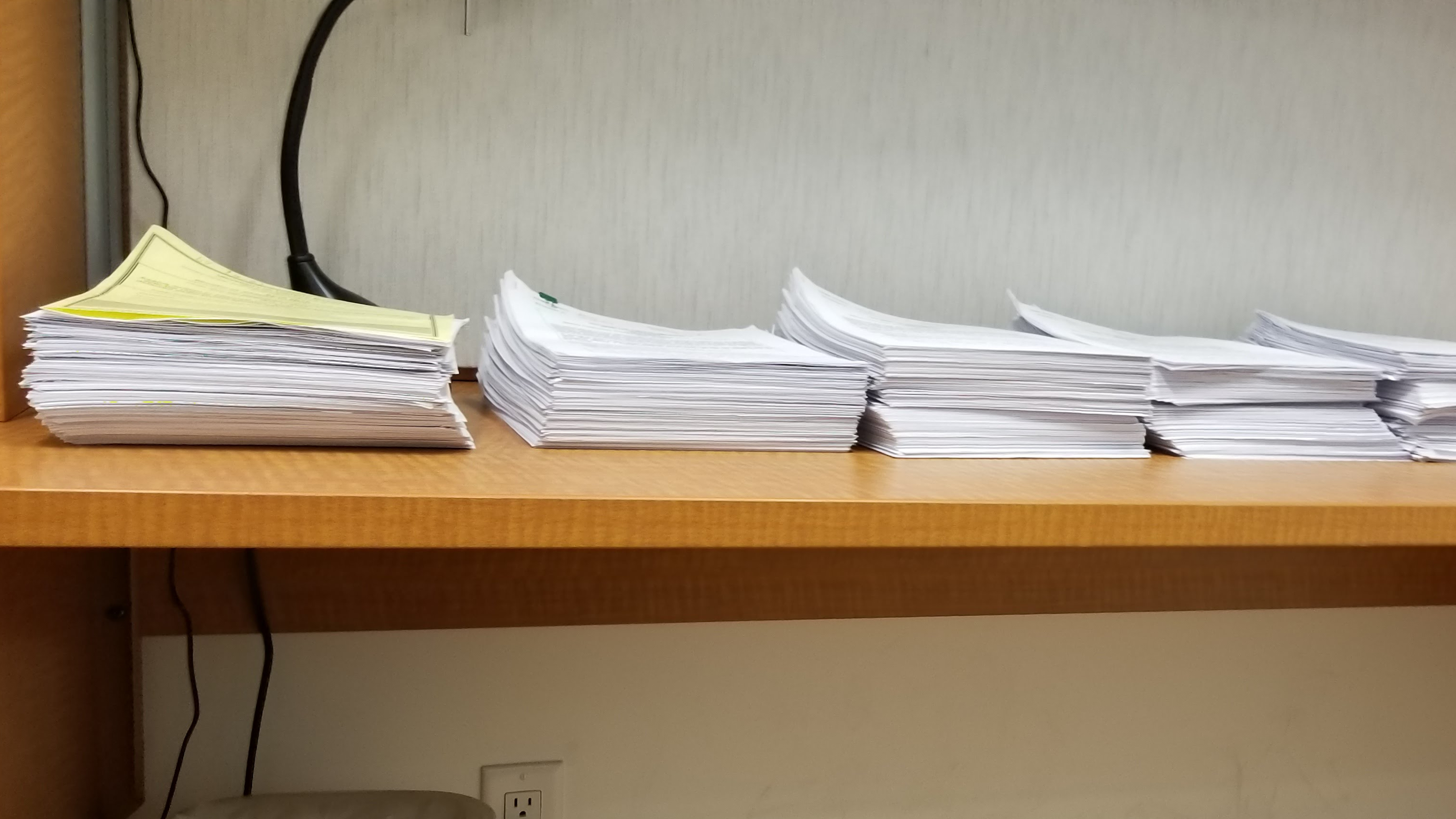 Five piles of test papers on a brown desk.